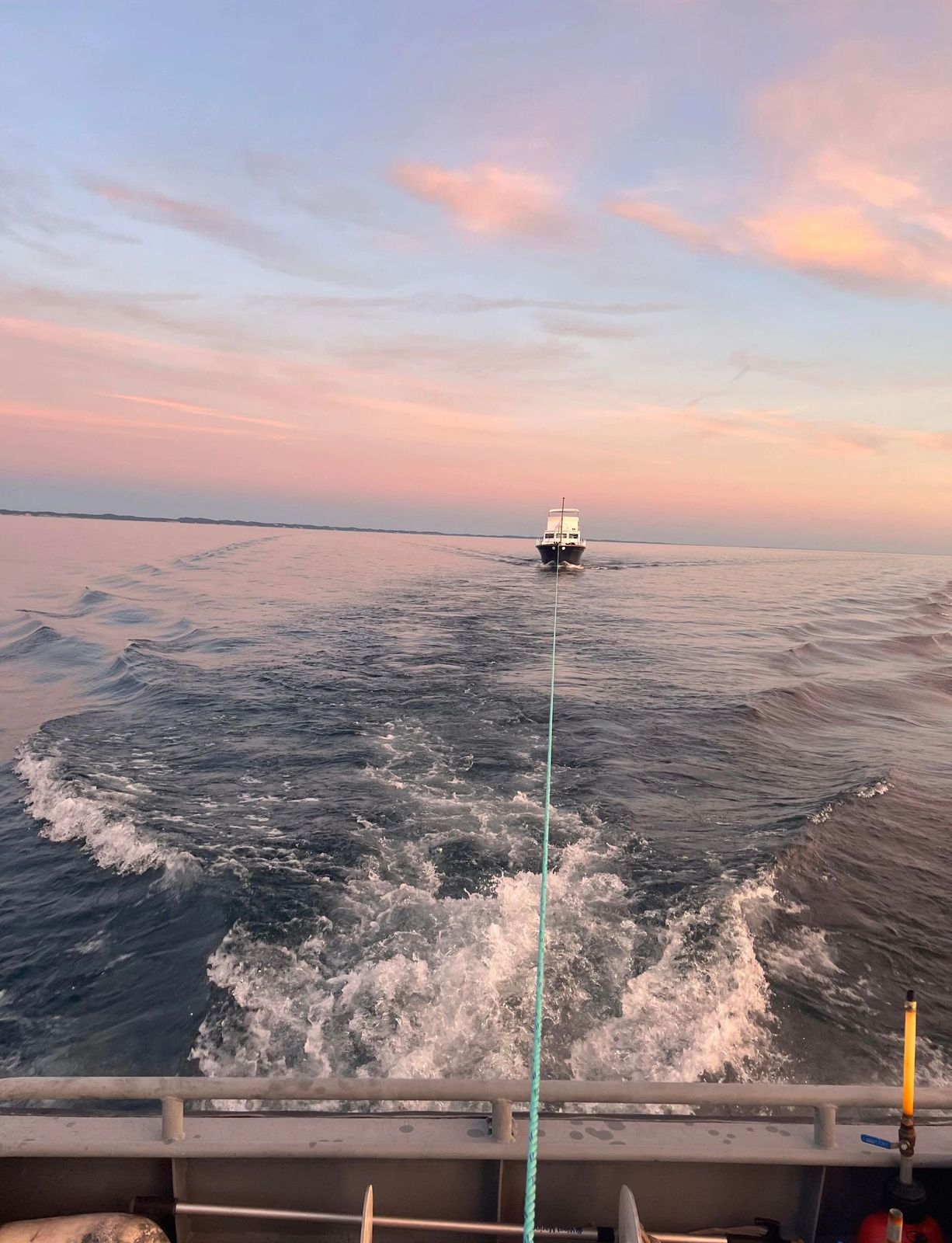 A tow line extending from the foreground boat to a vessel in the distance at golden sunset.