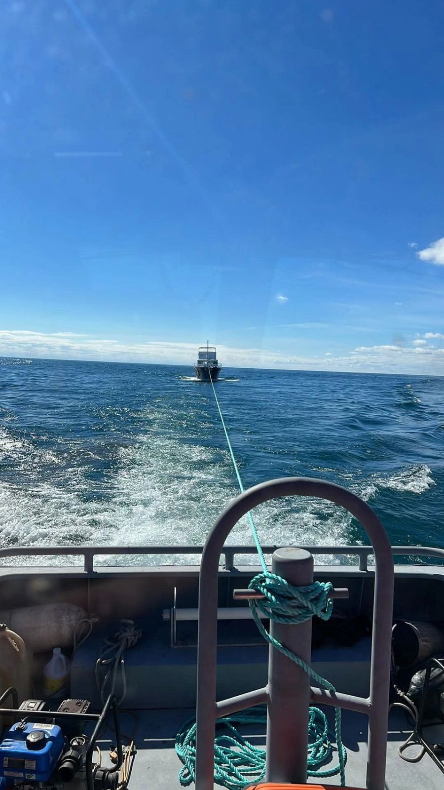 View from the helm of a towing boat with another vessel being towed in the distance across open blue water.