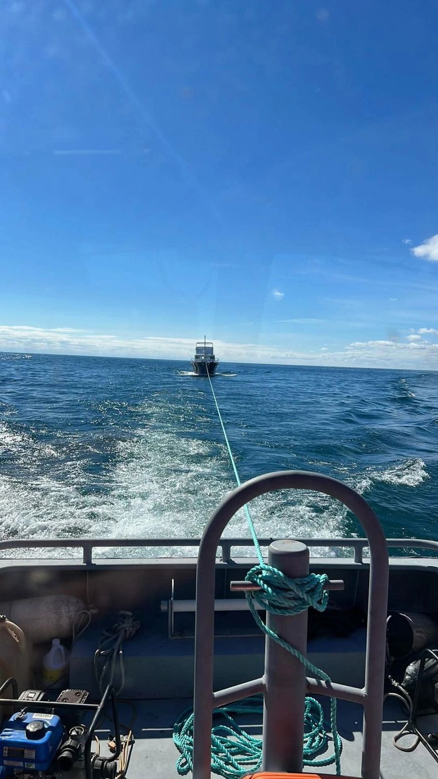 View from the helm of a towing boat with another vessel being towed in the distance across open blue water.