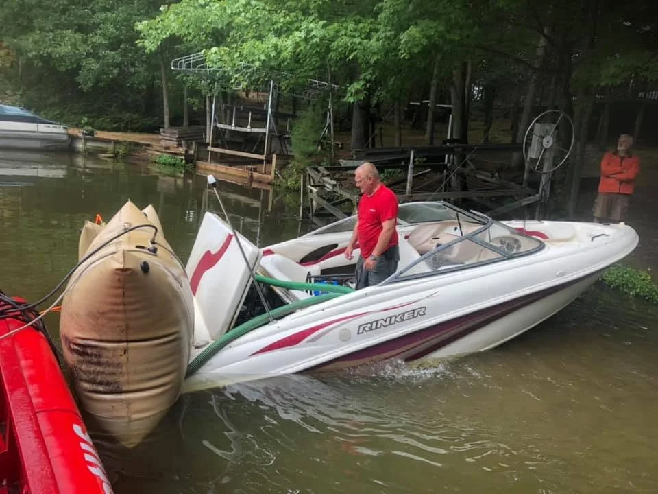A boat coming back up to the surface alongside a lift bag, with a crew member at the helm and H2O Boat Tow's towboat alongside.