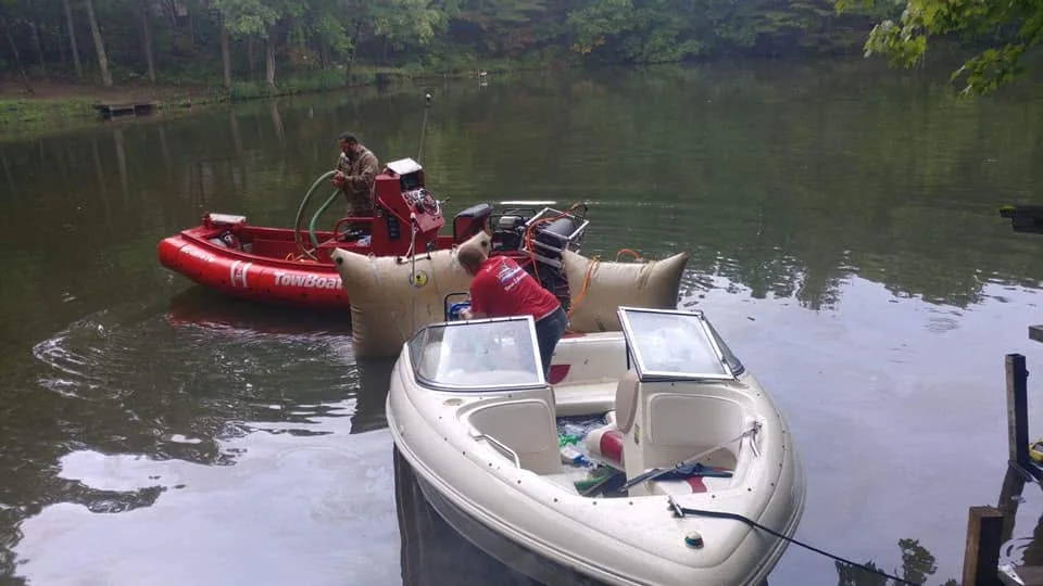 TowBoatUS crew running a pump from the towboat while a lift bag works alongside a recovered boat on the water.
