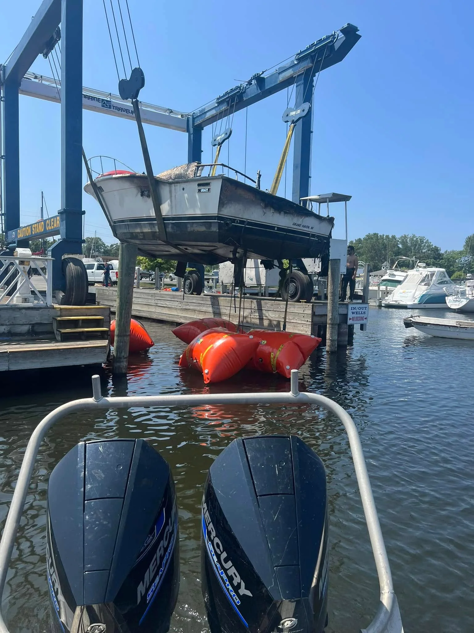 A crane lifting a boat clear of the water with lift bags floating in the water below.