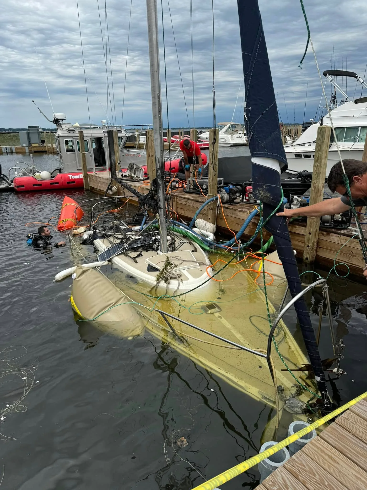 Lift bags set on the deck of a partially submerged sailboat at the dock, with H2O Boat Tow's towboat standing by.